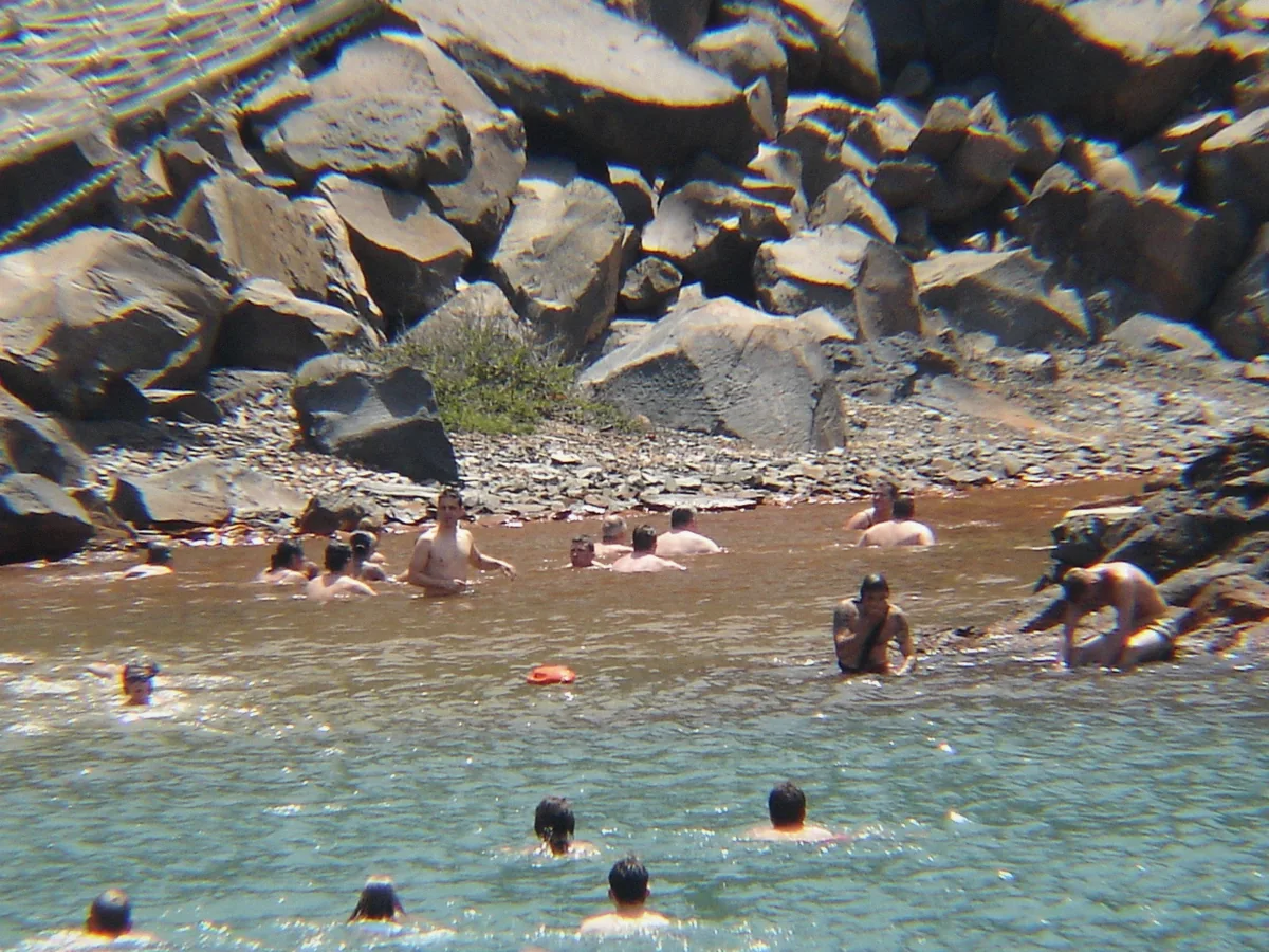 Swimmers in the rust-coloured water of the Palea Kameni hot springs during a Santorini boat tour, Greece