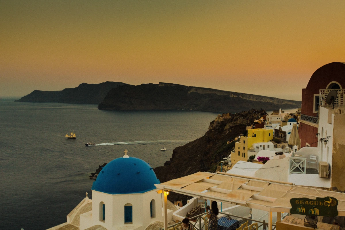 Blue dome and bell tower above the caldera cliffs of Oia at dusk during a Santorini sunset boat tour, Greece